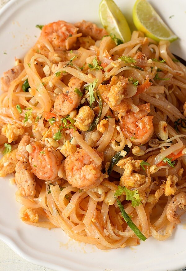 a white plate with authentic pad thai recipe with crushed peanuts ,beans,chicken and shrimp